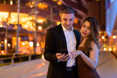 Portrait of couple using phone outdoors at night in the city at Bangkok Thailandの写真素材