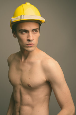 Young handsome man construction worker shirtless against gray backgroundの写真素材