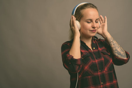 Young beautiful woman with blond hair listening to music against gray background
