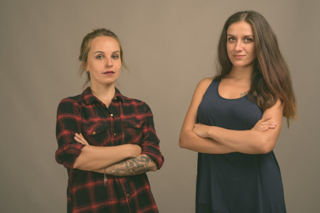 Two young beautiful woman friends against gray backgroundの写真素材