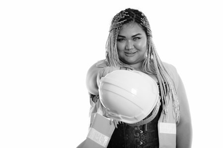 Young happy fat Asian construction woman smiling while pointing safety helmet at cameraの写真素材