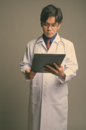 Young handsome Asian man doctor wearing eyeglasses against gray backgroundの写真素材