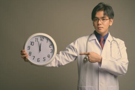 Young handsome Asian man doctor wearing eyeglasses against gray backgroundの写真素材