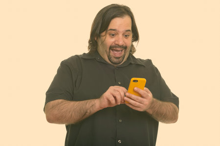 Happy fat Caucasian man laughing while using mobile phoneの写真素材