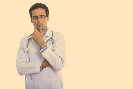 Studio shot of young handsome man doctor thinking while looking downの写真素材