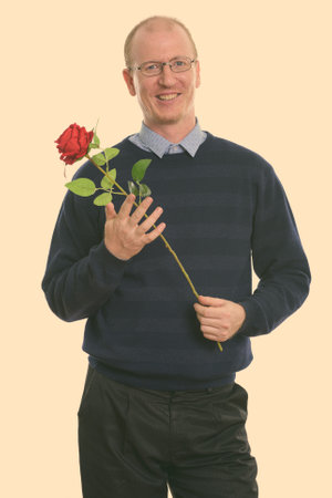 Studio shot of happy man smiling while holding red rose ready for Valentines dayの写真素材