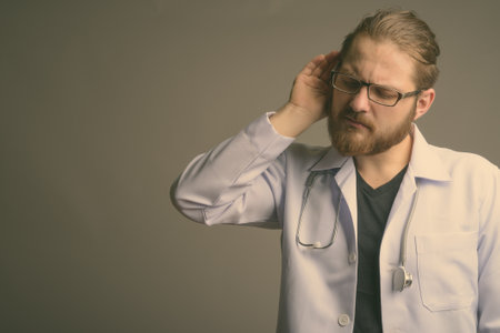 Young bearded man doctor against gray backgroundの写真素材