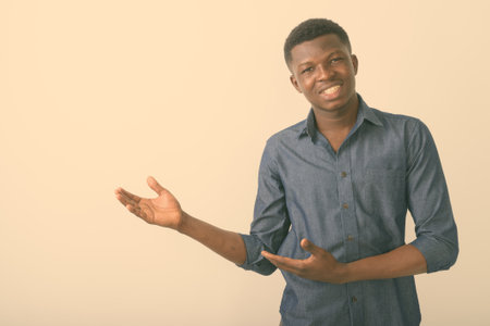 Studio shot of young happy black African man smiling while showing something against white backgroundの写真素材