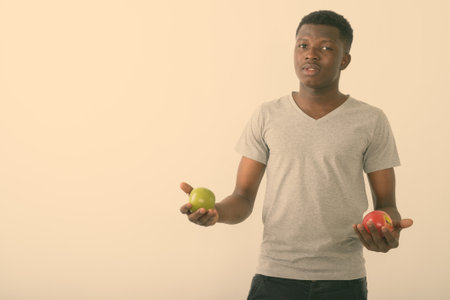 Studio shot of young black African man holding red apple and green apple against white backgroundの写真素材