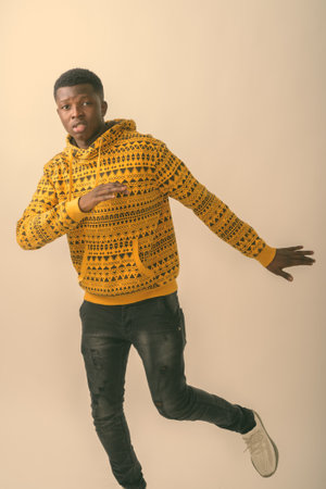 Studio shot of young black African man standing while posing with leg raised against white backgroundの写真素材