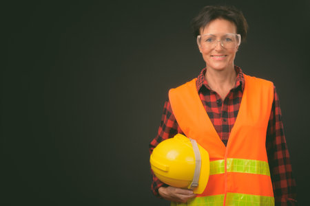 Mature beautiful woman construction worker with short hair against black backgroundの写真素材