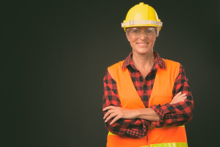 Mature beautiful woman construction worker with short hair against black backgroundの写真素材