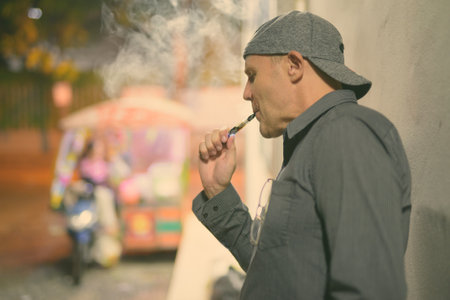 Mature man smoking electronic cigarette in the streets at nightの写真素材