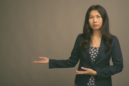Asian woman wearing blue dress and cardigan sweater against gray backgroundの写真素材