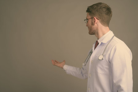 Young handsome man doctor wearing eyeglasses against gray background