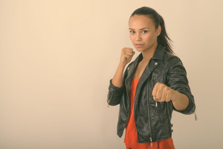 Studio shot of young Asian woman wearing leather jacket ready to fight against white background
