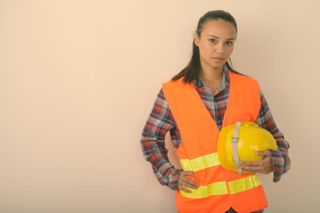 Studio shot of young Asian woman construction worker holding hard hat against white backgroundの写真素材