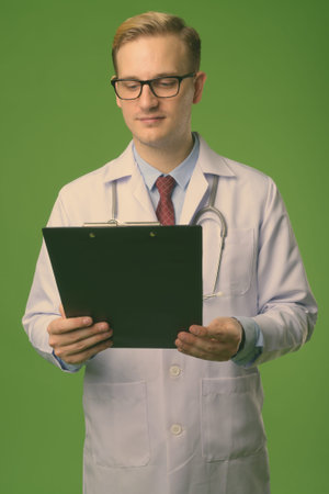 Young handsome man doctor with blond hair against green backgroundの写真素材