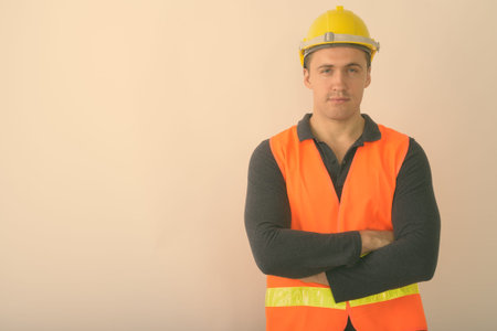 Studio shot of young muscular man construction worker with arms crossed against white background