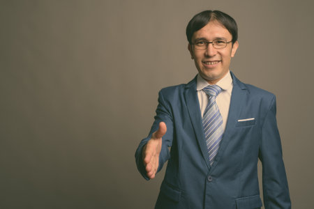 Young Asian businessman against gray backgroundの写真素材