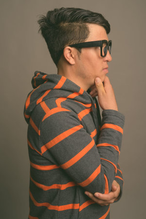 Young Asian nerd man wearing hoodie against gray background