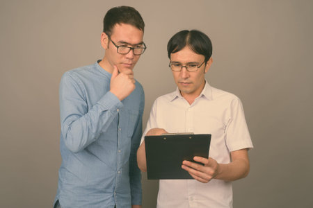 Two young Asian businessmen wearing eyeglasses together against gray background