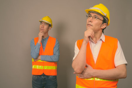 Two young Asian men construction worker together against gray backgroundの写真素材