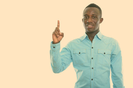 Studio shot of young happy black African man smiling while pointing finger upの写真素材