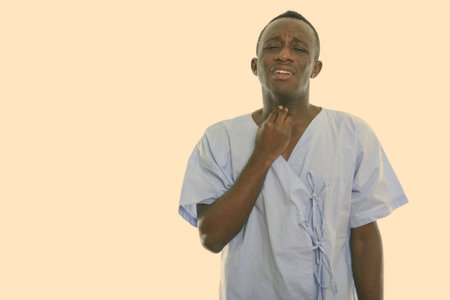 Studio shot of young black African man patient having sore throatの写真素材