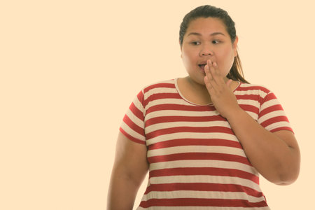Studio shot of young fat Asian woman looking shocked while covering mouth