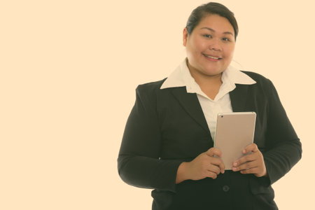 Studio shot of young happy fat Asian businesswoman smiling while holding digital tabletの写真素材