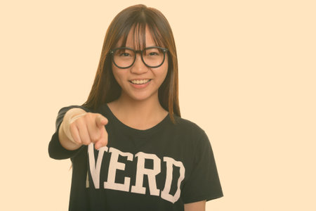 Young happy Asian nerd teenage girl smiling and pointing finger at camera
