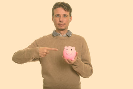Handsome Caucasian man holding piggy bank while pointing fingerの写真素材