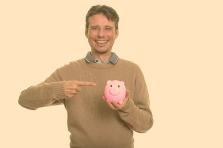 Happy Caucasian man holding piggy bank while pointing fingerの写真素材