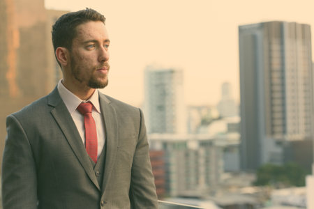 Young handsome Caucasian businessman thinking and looking away in rooftop at city in Bangkok Thailandの写真素材
