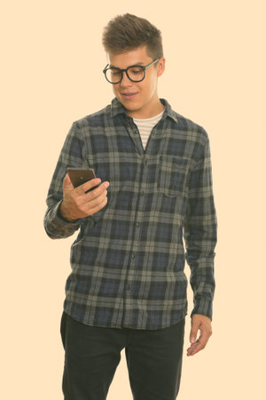 Studio shot of young handsome man standing while using mobile phone