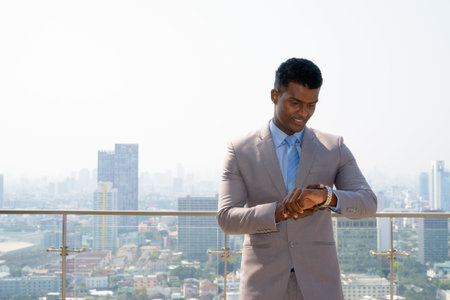 Portrait of handsome young African businessman wearing suit checking time from wrist watch