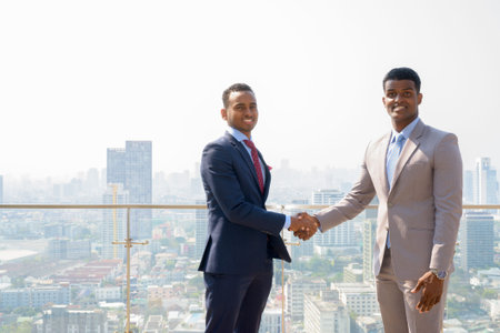Portrait of two African businessman smiling and having handshake while looking at camera