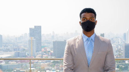 African businessman with face mask for protection at rooftop looking at camera