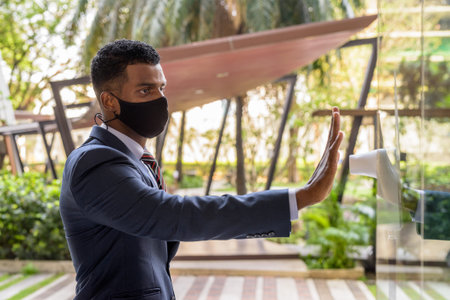 African businessman wearing face mask for protection and measuring body temperature before entering...