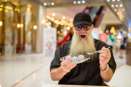 Happy man sitting in shopping mall and eating ice creamの写真素材