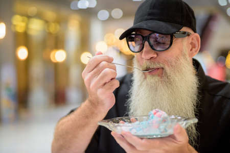 Man sitting in shopping mall and eating ice cream enjoying with eyes closedの写真素材