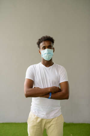 African man wearing face mask against plain wall background with arms crossedの写真素材