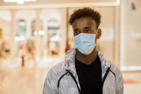 Portrait of handsome black African man wearing face mask in shopping mall while thinking