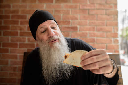 Portrait of mature man with long gray beard holding tacoの写真素材