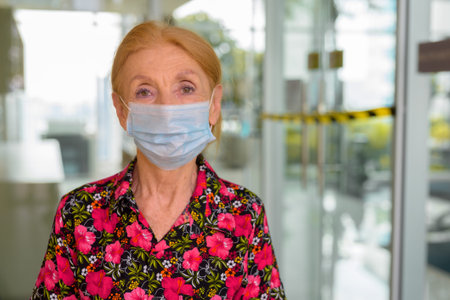 Indoors portrait of senior woman wearing disposable medical face mask against closed gym during...