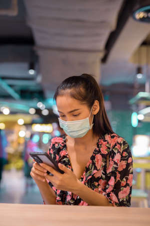 Woman wearing face mask for protection against virus while using mobile phone at restaurantの写真素材