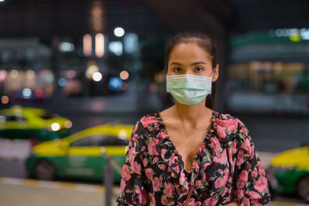 Woman wearing face mask for protection against virus while waiting taxi at nightの写真素材