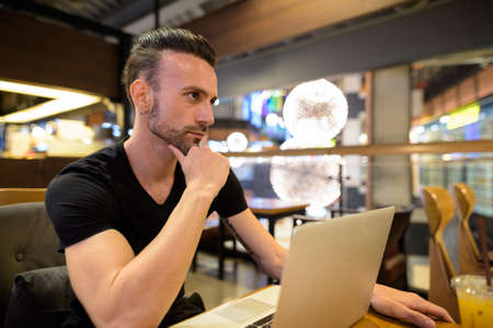 Man sitting at coffee shop using laptop computer and thinkingの写真素材