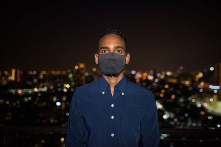 African businessman outdoors at rooftop wearing face mask at nightの写真素材
